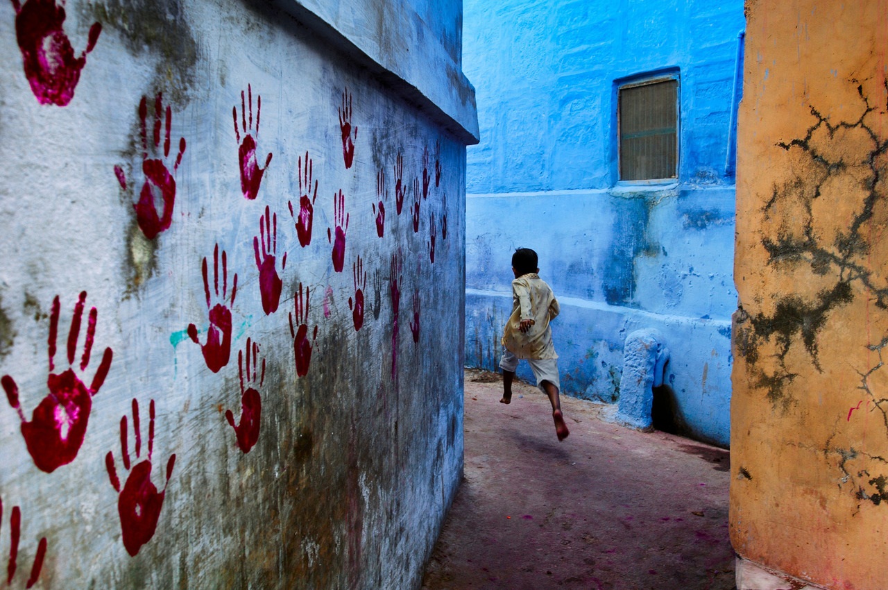 Boy in mid-flight, Jodhpur, India, 2007 At the foot of the vast Mehrangarh Fort, one can find the Blue City, a small tightly knit maze of houses located towards the north of Jodhpur. In one of the narrow alleyways a boy flees McCurry's camera. Balancin